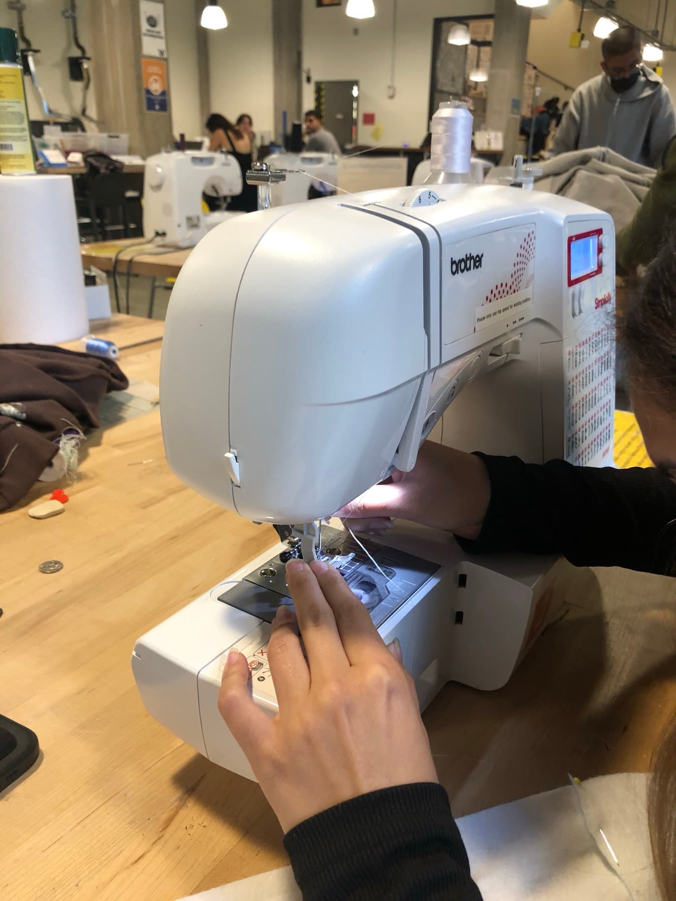 Hands guiding fabric through a Brother sewing machine in a makerspace.