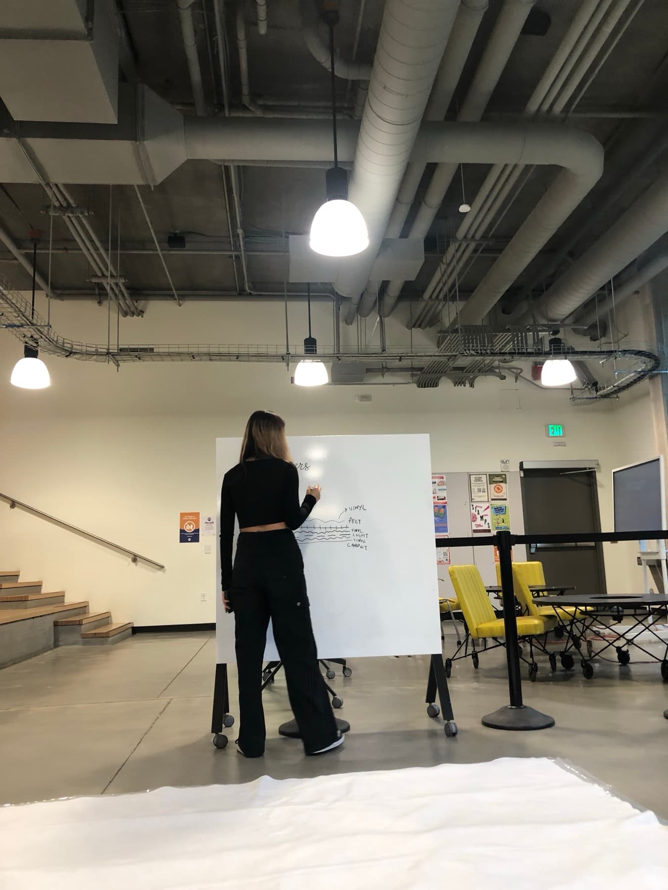 A team member at a whiteboard sketching the mat's cross-section: vinyl, felt, lights, vinyl, carpet.